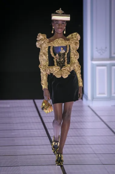 Želiš li outfit u kojemu ćeš izgledati kao remek-djelo iz muzeja? Ne brini, Moschino ima odgovor. Crna haljina sa zlatnim rukavima i obrubom neodoljivo podsjeća na kakvu sliku iz muzeja, što dodatno potvrđuje i detalj zlatne lampe na glavi modela.