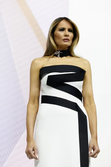 Melania je oduševila sve prisutne bijelom satenskom haljinom bez naramenica s crnim detaljima u obliku linija koje omotavaju korzet. A kako bi upotpunila svoj izgled, nosila je odgovarajući crni satenski choker s srebrnim privjeskom i imala kosu u dugim, opuštenim valovima. Haljina je kreacija dizajnera Herve Pierre. 
