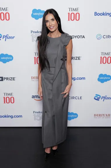 Demi Moore nosi sofisticiranu sivu haljinu koja ima elegantne naborane detalje sa strane, stvarajući dinamičan izgled. Haljina ima moderni kroj s minimalističkim pristupom, dok asimetrični detalji dodaju dozu kreativnosti i sofisticiranosti. Ovaj stylish look upotpunjen je crnim, lakiranim štiklama, stvarajući savršen balans između klasične elegancije i suvremenog dizajna.