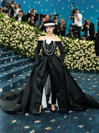 Jennie je zablistala u elegantnom izdanju Chanela, koje je na profinjen način interpretiralo temu večeri &quot;tailored for you&quot;. Nosila je crni kombinezon bez naramenica, izrađen od luksuzne kože i satena, ukrašen bisernim gumbima. Look je upotpunila s dva niza bisera i kultnom bijelom kamelijom – ikonskim Chanel detaljem.